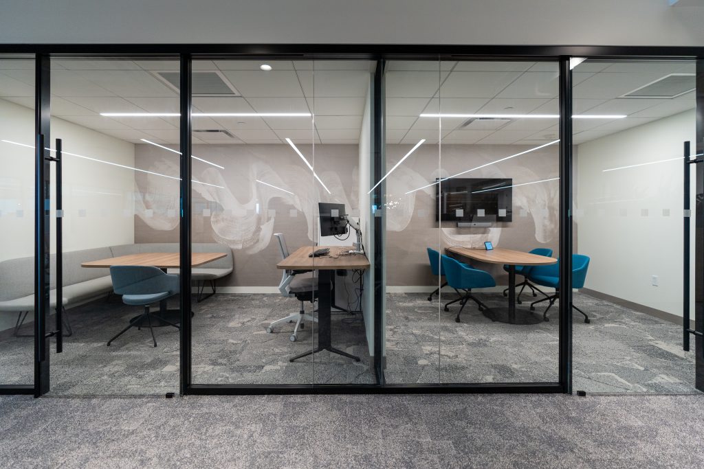 Glass wall interior with matte black finishes and sliding doors in meeting rooms and private offices with desks and chairs.  