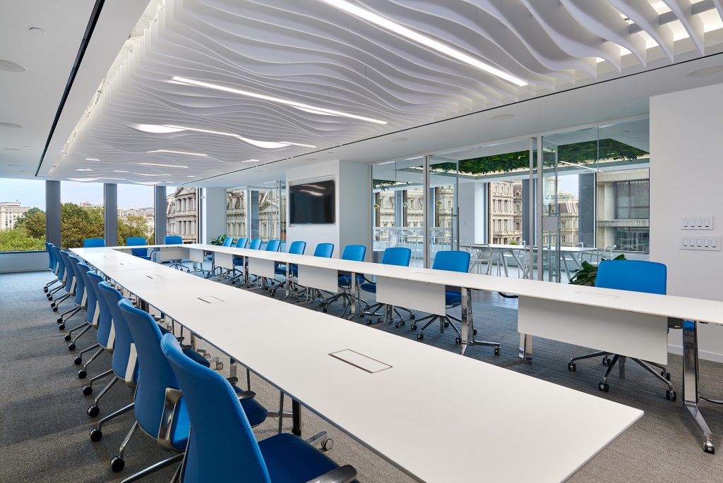 Executive boardroom with glass interiors and large conference room table with blue chairs.